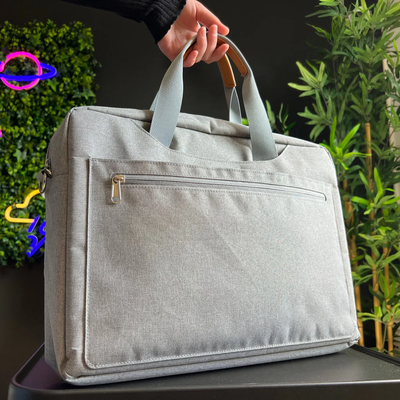 Gray waterproof Oxford fabric laptop sleeve tote bag with reinforced handles and front zipper pocket, shown as a handheld product shot in a natural lifestyle setting, designed for carrying and protecting portable monitors or laptops during travel and daily use.